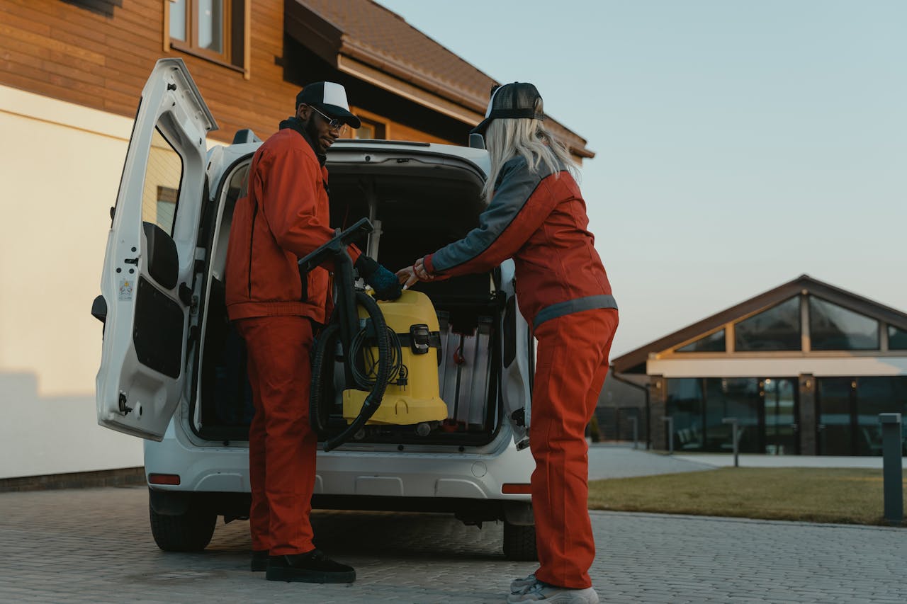 gallery-03 Two cleaners loading a vacuum into a van outside a modern building at dusk.